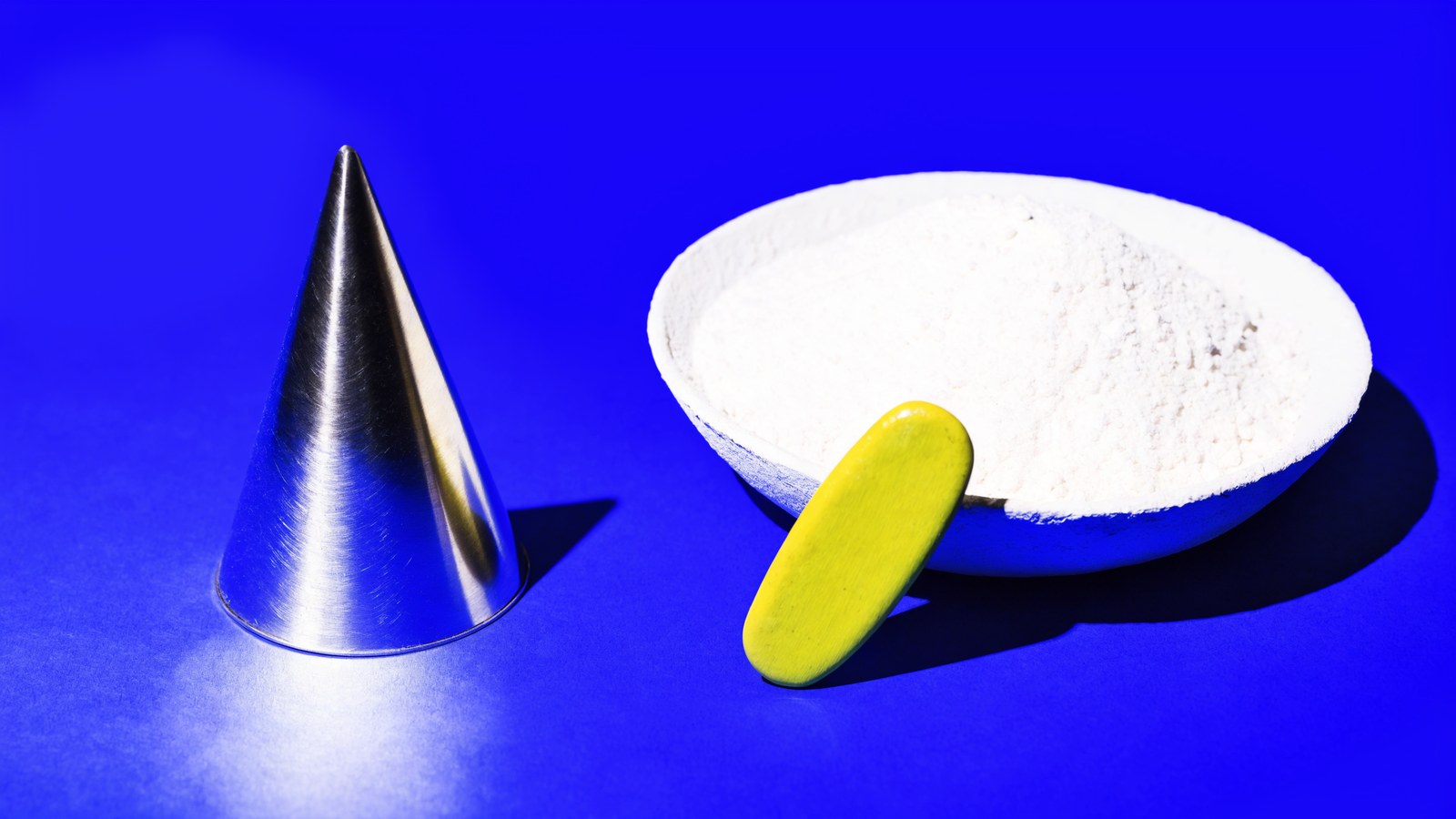 A steel cone beside a dish of fine dust on cobalt with a chartreuse marker